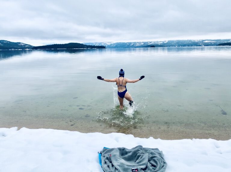 Female winter swimmer running into lake with snow on banks